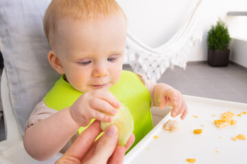 Hand of mom giving slice of fresh vegetable to baby, feeding daughter during lunch time. First solid food or child care at home concept