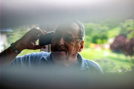 Senior man using Smart phone, light effect. Portrait through the glass of man talking on mobile. Technology concept.