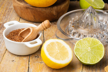 Close-up of half lemon, lime, brown sugar, juicer and wooden bowl with lemons, black background,...
