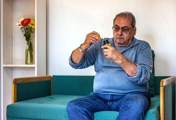 Senior man taking medicine at home. Older man taking daily medicine to consume. Man pouring a pill from into hand.