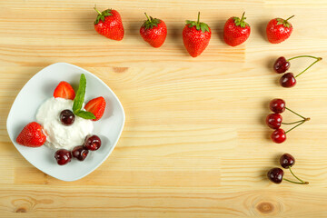 Ice cream dessert with strawberries and cherries in a plate on a wooden table and next to the berries. Copy space.