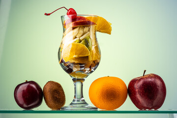 fruit salad of fresh fruits and berries in a transparent glass on a gradient background