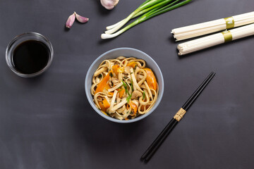 Udon noodles with chicken, soy sauce, bamboo sticks and fresh ingredients on a black background. Japanese cuisine.