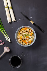 Fototapeta na wymiar Udon noodles with chicken, soy sauce, bamboo sticks and fresh ingredients on a black background. Top view. Japanese cuisine.