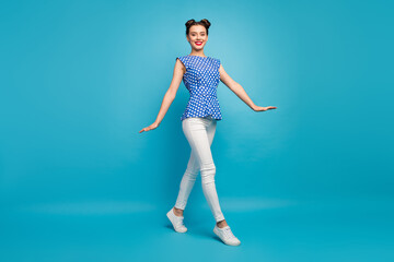 Full length profile photo of pretty funny lady good mood walking down street summer warm sunny day wear dotted blouse white pants shoes isolated blue color background