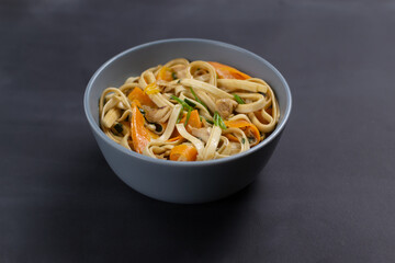 Udon noodles with chicken in a gray bowl on a black background. Close up. Minimalism. Japanese cuisine.
