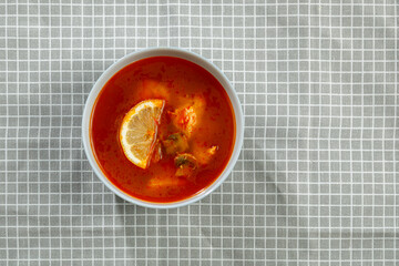 Traditional Tom Yum soup with chicken in a plate on a tablecloth on a linen napkin.