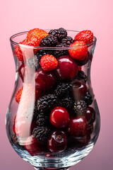 mix of cherries, strawberries and mulberries in a transparent glass on a gradient background