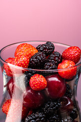 mix of cherries, strawberries and mulberries in a transparent glass on a gradient background