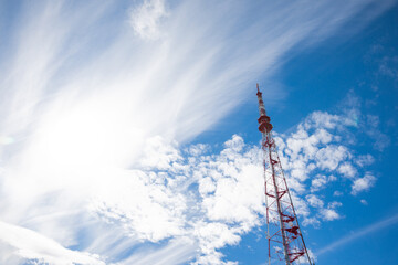Obraz premium red tall television tower on a background of blue sky and clouds 