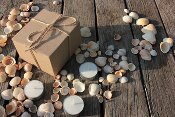 Fototapeta na wymiar Brown gift box, tea candles, and seashells on the natural weathered old wooden background with copy space. Top view. Summer birthday present 