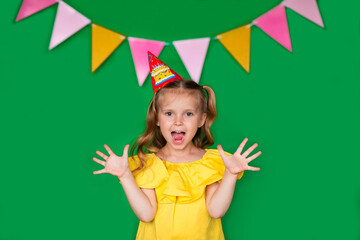 Young birthday girl in yellow blouse with cap laughing on green background with copy space. Very happy.