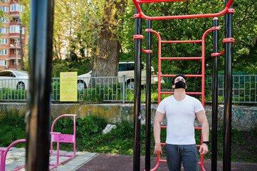 Portrait sports arabian man in black medical face mask doing workout exercises in outdoor gym place during coronavirus quarantine.