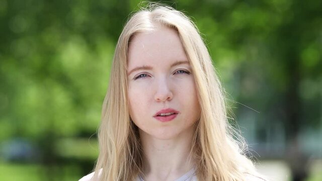 Portrait of a cute young blonde girl with hair flowing in the light wind on the natural background of the park on a sunny summer day

