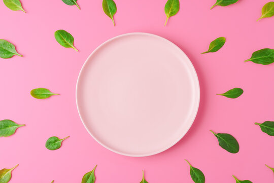 Spinach leaves around empty plate on pink background. Green healthy eating concept. Top view, copy space
