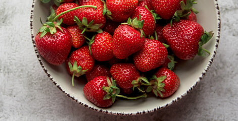 Close up top view of fresh ripe organic strawberry in ceramic  bowl on light gray background. Organic fruit diet. Healthy vegetarian nutrition