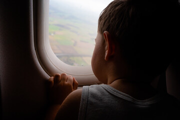 2 years old boy looking out from the window of the plane - rear view
