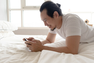 Happy Asian man stays home and play mobile game in his apartment.