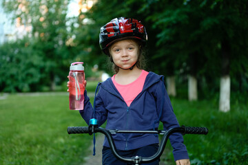 Little girl drinking water by the bike. Child in helmet riding a bicycling.
