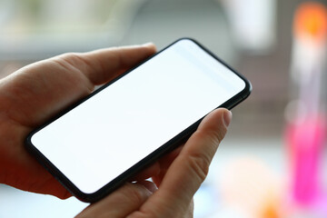 Close-up of person holding modern smartphone with white screen. Adult using mobile phone for searching information. Text on display. Technology and spare time concept