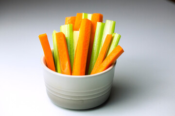 close up filled frame isolated shot of party snack food. A white bowl of crunchy orange carrot and juicy green celery sticks on a white background