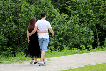 Hugging couple walks in a summer park. Guy and girl in love, romantic date on nature, happy lovers
