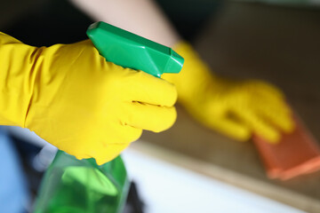 Close-up of person using cleaning product and wearing bright yellow gloves. Male holding rag. Housekeeper. Professional cleaning service and cleanliness at home concept