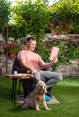 Obraz premium Handsome man relaxing on a chair and using tablet pc in the garden