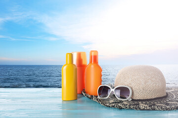 Set of sun protection products and stylish accessories on wooden table near sea