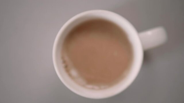 Adding a teaspoon of sugar into a mug of light  espresso coffee with milk, birds eye view, 6fps slow motion 4K