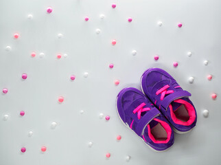 Flatlay of violet pink childrens sneakers with pink and white balls at peach background