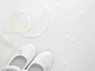 Flat lay with pair of white baby lacquered girls shoes with beige ribbon and white balls at white background