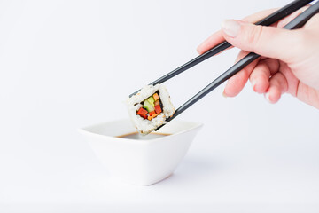 Female dipping tasty sushi makaki or uramaki with chopsticks into bowl with soy sauce on white...