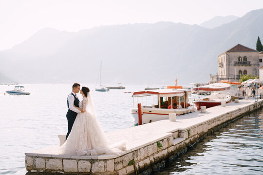 Wedding couple on a boat pier with views of the mountains and sunset light. Fine-art wedding photo in Montenegro, Perast.