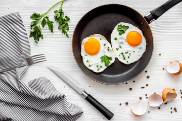Fried eggs on frying pan on white table top-down