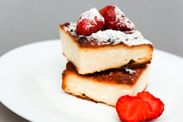 Cottage cheese casserole portion with strawberries and powdered sugar on a grey background. concept of Breakfast.
