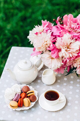 A cozy romantic breakfast in the open air. Peony flower vase, teapot and cup of tea, macaroon cake...