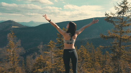 Athletic woman enjoys nature, clean air and beautiful views on the top of the mountain. Spreads her arms to the sides
