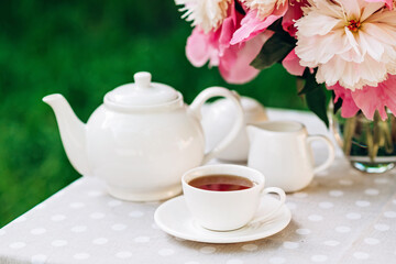 A cozy romantic breakfast in the open air. Peony flower vase, teapot and cup of tea on the table. Congratulations on mother's day or women's day. 