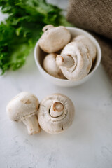 Champignon mushrooms in a white bowl with herbs on the table close-up.