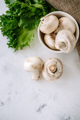 Champignon mushrooms in a white bowl with herbs on the table close-up.