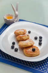 Syrniki or cottage cheese pancakes with blueberries and honey on white plate with blue napkin on kitchen table. Healthy breakfast, diet concept.