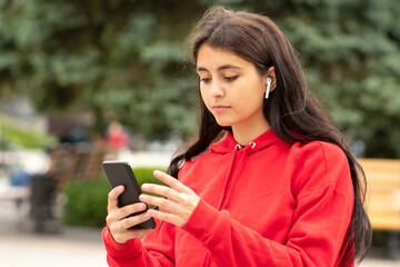 A woman walks down the street in headphones and carefully looks into her smartphone