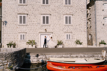 Fototapeta na wymiar Fine-art wedding photo in Montenegro, Perast. The bride and groom are dancing against the backdrop of an old white house and moored kayaks.