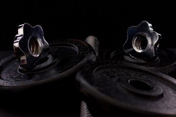 Black metal dumbbell for fitness with a chrome handle, on a black background.