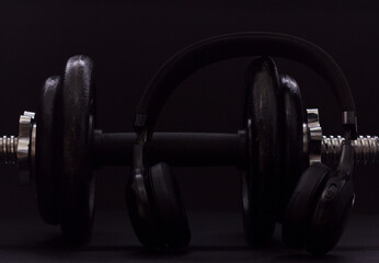Fototapeta na wymiar Black metal dumbbell for fitness with headphones, on a black background.