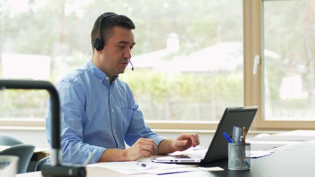 remote job, technology and business concept - happy smiling middle-aged man with headset and laptop computer having video or conference call at home office