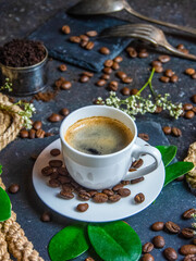 White coffee cup, roasted coffee beans and green leaves on dark background    