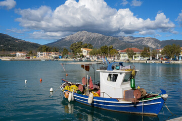 Fototapeta na wymiar Traditional Greek fishing boat in Vasiliki harbor with a view of the town and mountian in the background with blue sky clouds.