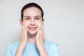 A smiling beautiful girl's face in acne uses a foaming cleanser. Teenage skin care concept, copy space